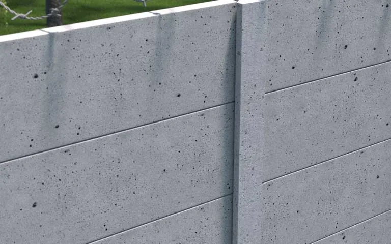 Siva industrijska betonska ograda sa glatkim panelima i bodljikavom žicom iznad