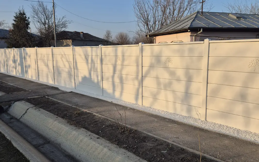 Betonska ograda sa glatkim panelima i reljefom stilizovanog drveta pored ulice