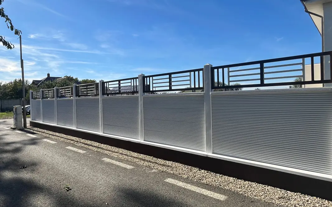 Bela betonska ograda sa metalnom rešetkom iznad panela, pored ulice